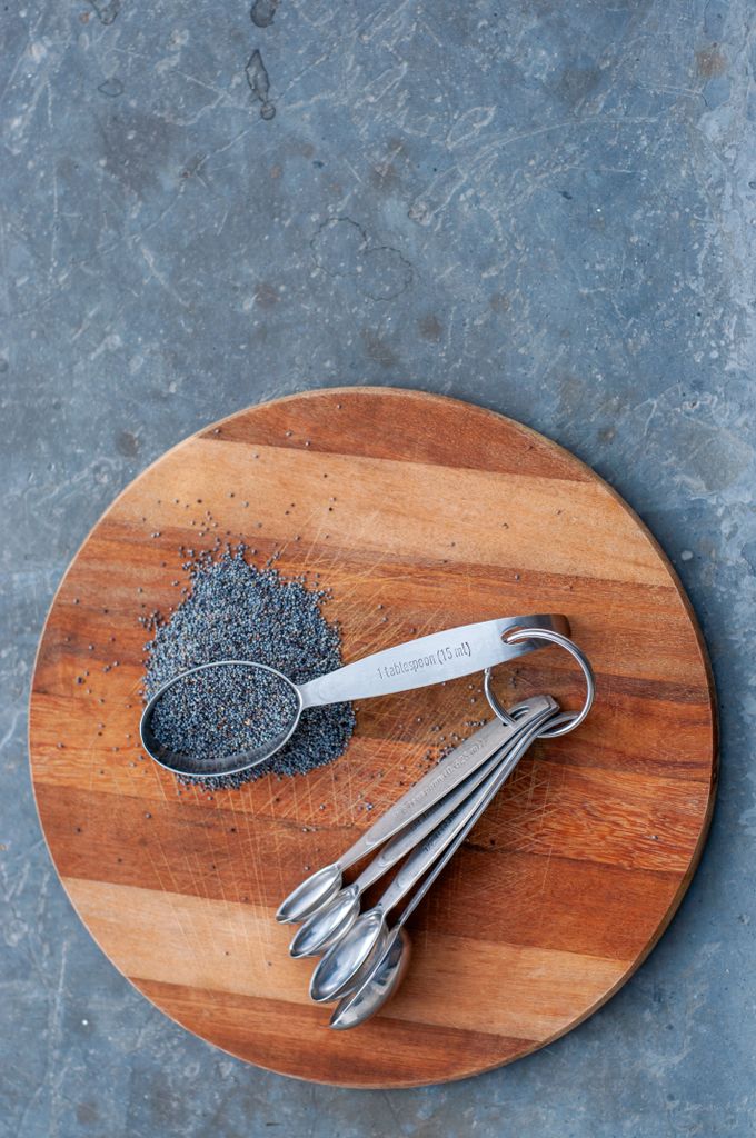 Stylish arrangement of poppy seeds and metal spoons on a wooden board.